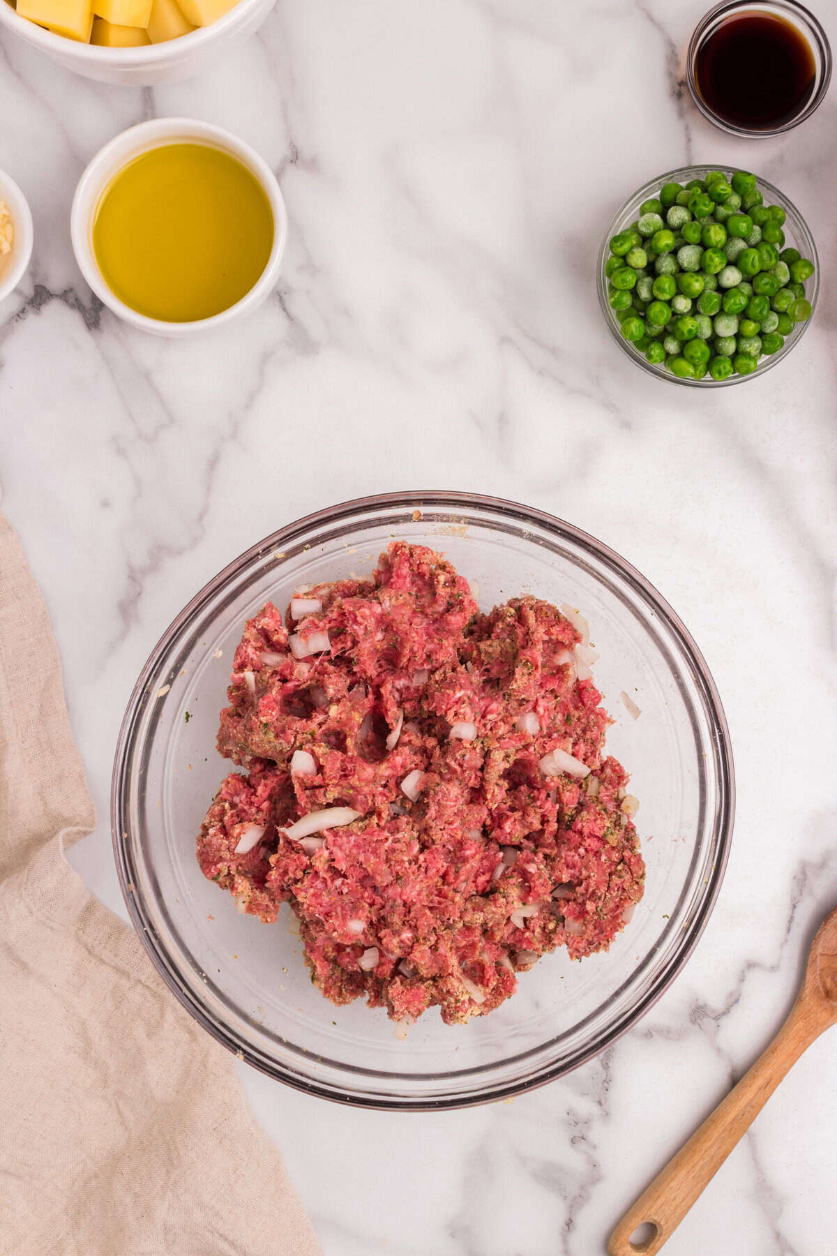 The meatball mixture has been combined thoroughly in the same glass bowl. The onions, breadcrumbs, and seasonings are evenly mixed with the ground meat.
