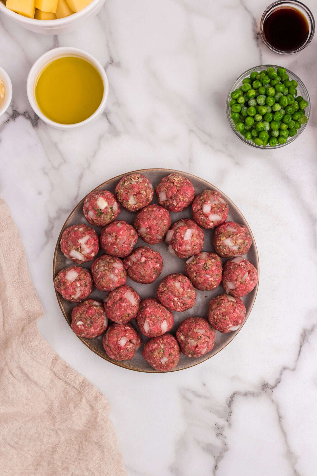 Formed raw meatballs are neatly arranged on a plate, ready for cooking. Each meatball is evenly shaped with visible bits of chopped onion and seasoning.