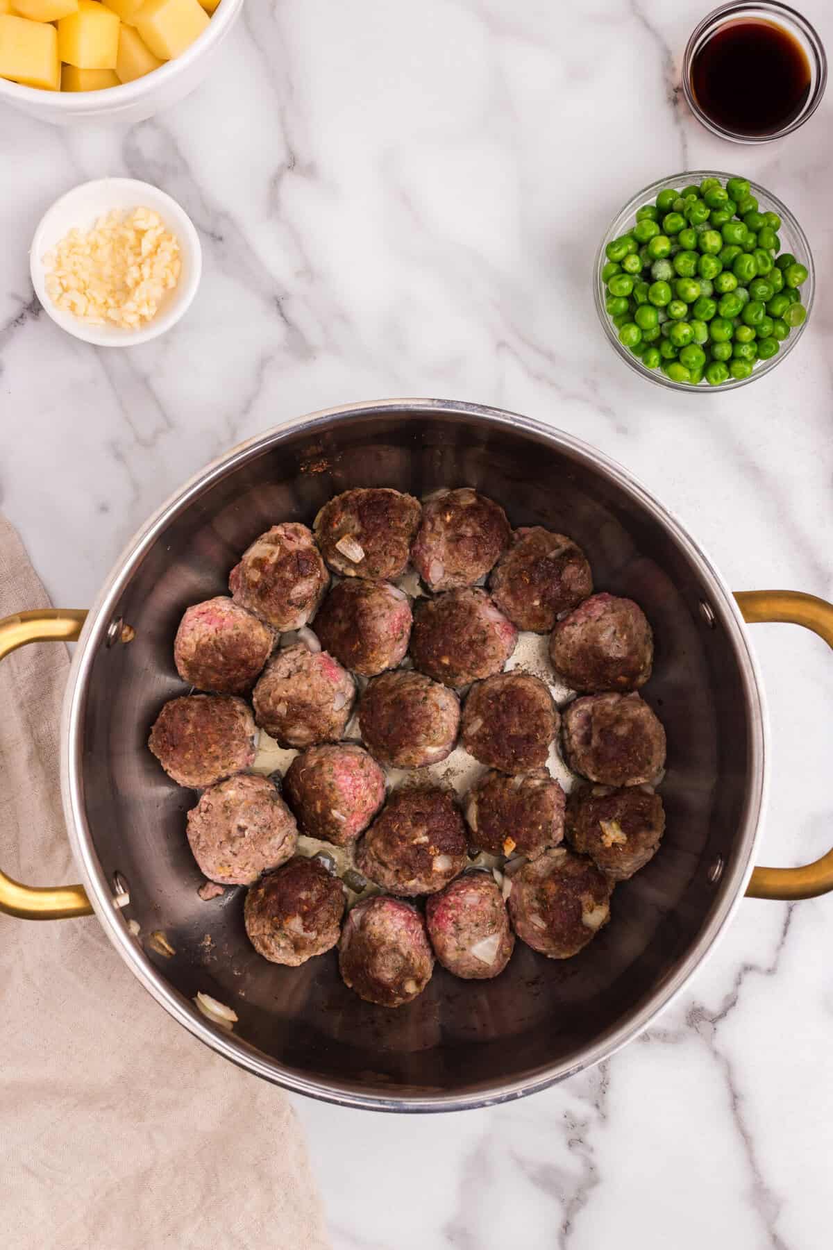 Meatballs are searing in a large pot, partially browned on the outside. Some pink is still visible, indicating the cooking process has just started.