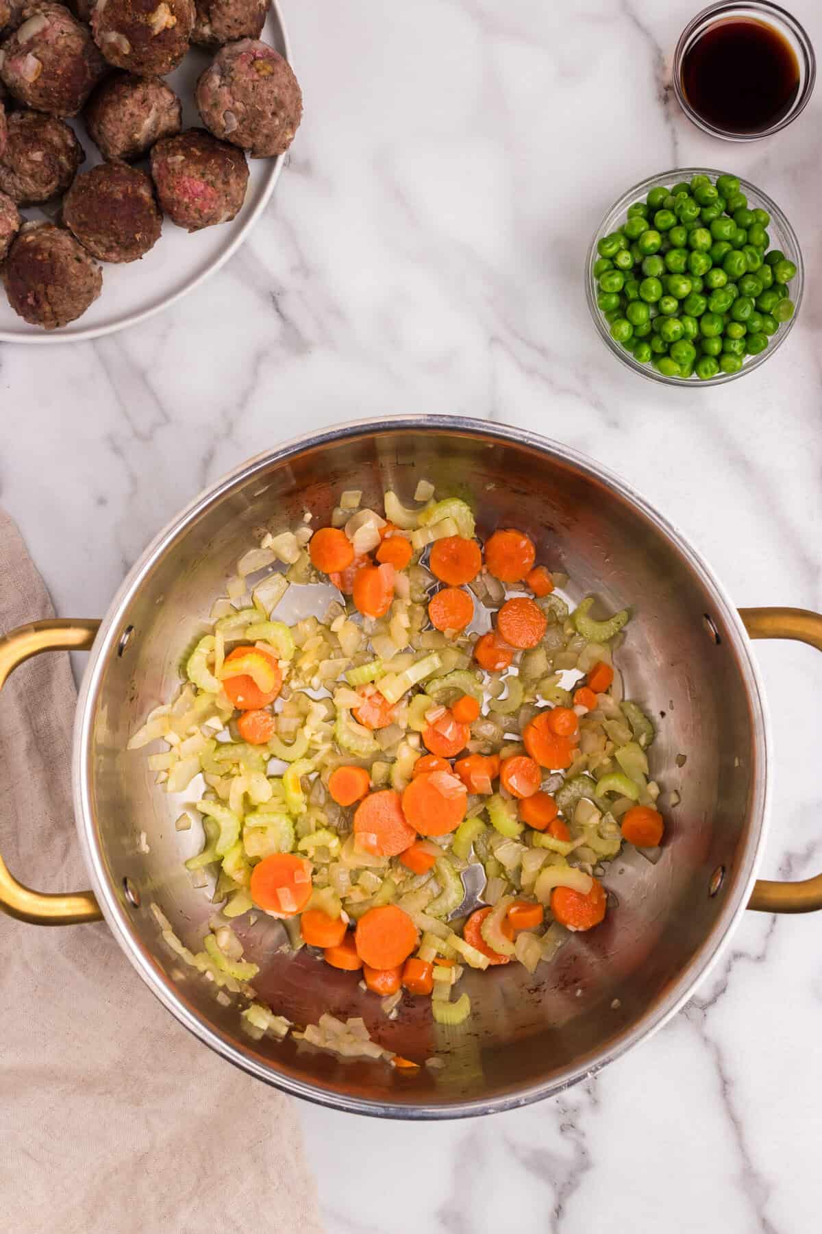 Chopped onions, carrots, and celery are being sautéed in the same pot after removing the meatballs, showing the preparation of the stew base.