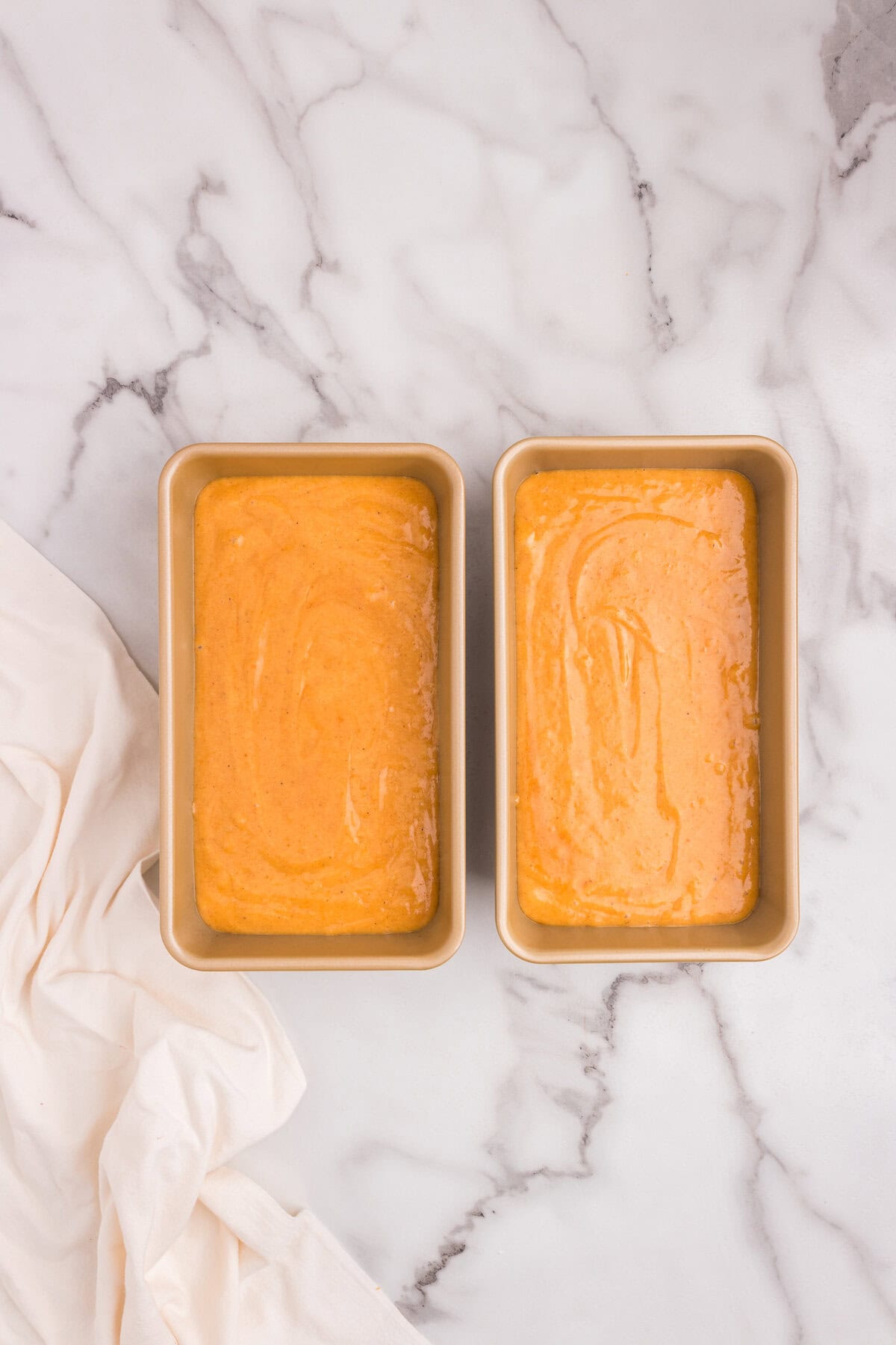 The pumpkin bread batter has been poured evenly into two greased loaf pans, ready to go into the oven.