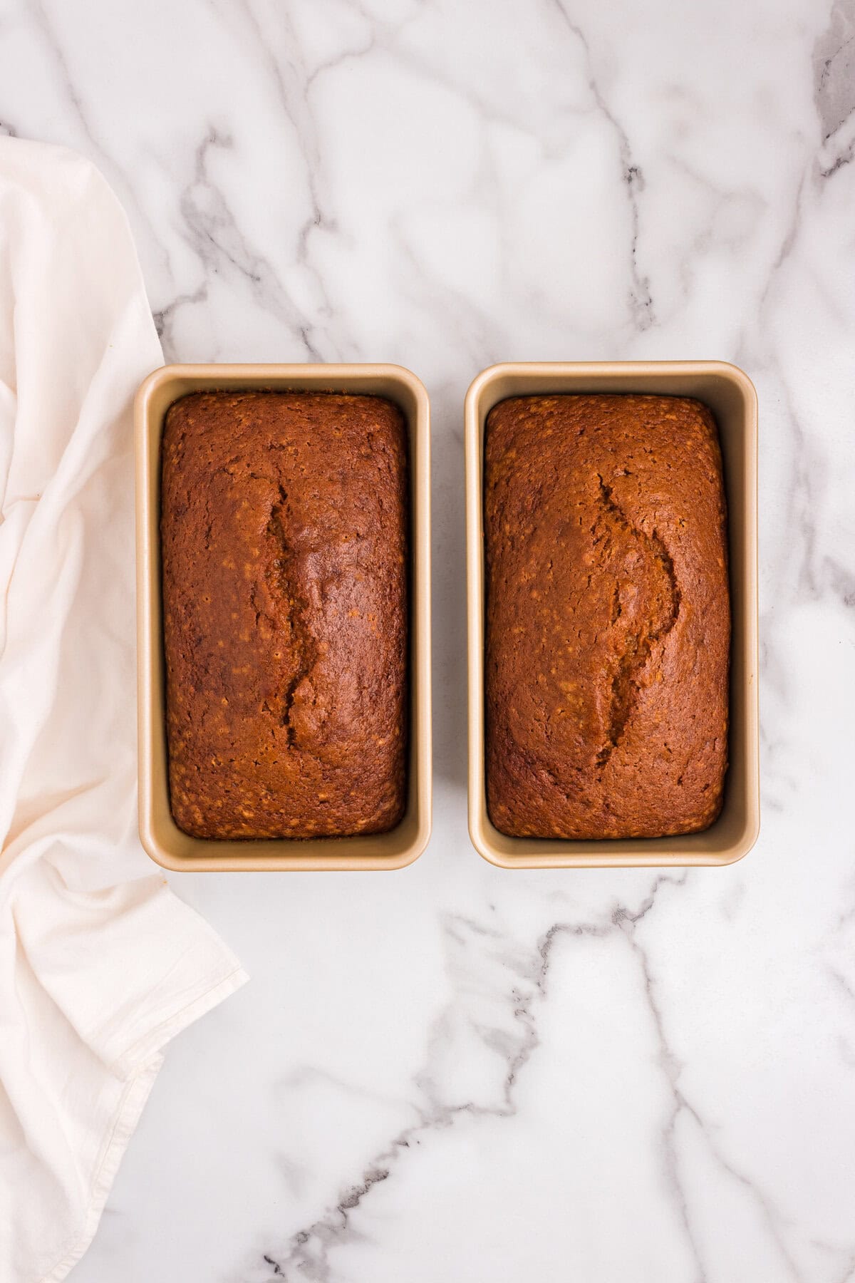 The baked pumpkin bread loaves have risen and browned perfectly in their pans, showing slight cracks on the top—indicating doneness.