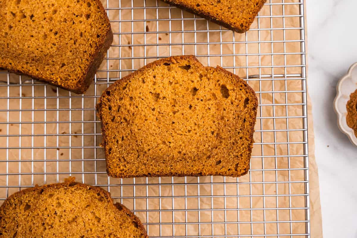 A close-up of a single slice of pumpkin bread on a wire cooling rack, showcasing its soft, moist crumb and golden-brown color.