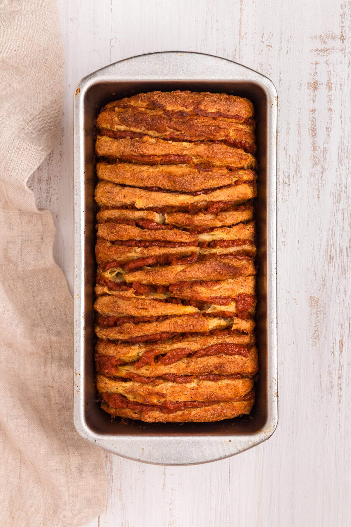 Baked pumpkin pull-apart bread in a metal loaf pan. The bread is golden brown with defined layers of cinnamon-sugar biscuits and pumpkin filling peeking through.