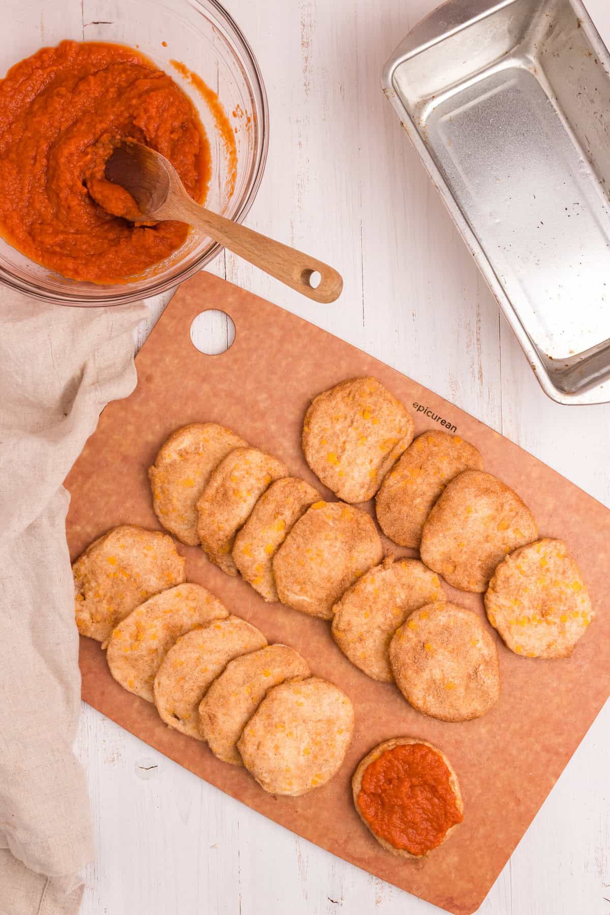 All biscuit rounds are now coated in cinnamon sugar. One round is topped with pumpkin filling, beginning the layering process. The loaf pan is ready on the side.