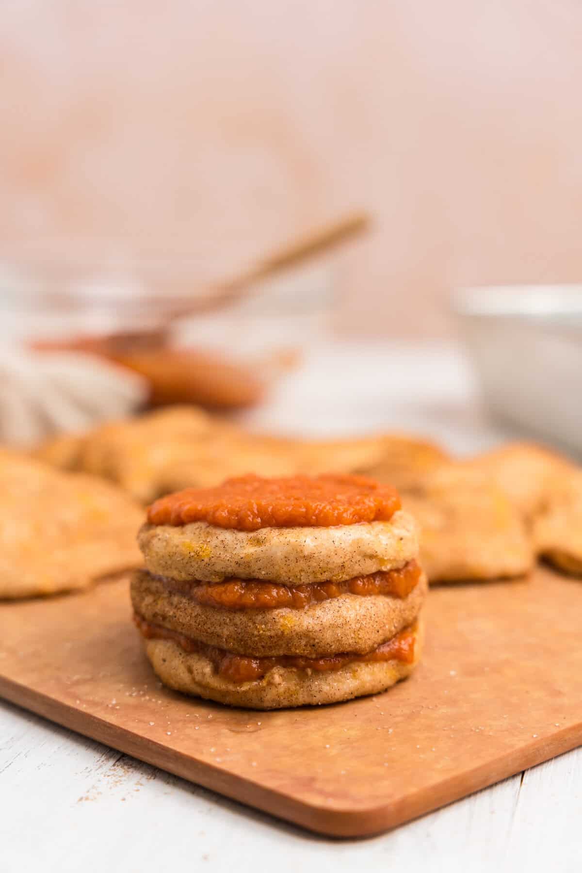A close-up of a stack of cinnamon-sugar-coated biscuit rounds layered with pumpkin filling on a cutting board. The layers are neatly stacked and ready to be assembled into the loaf.