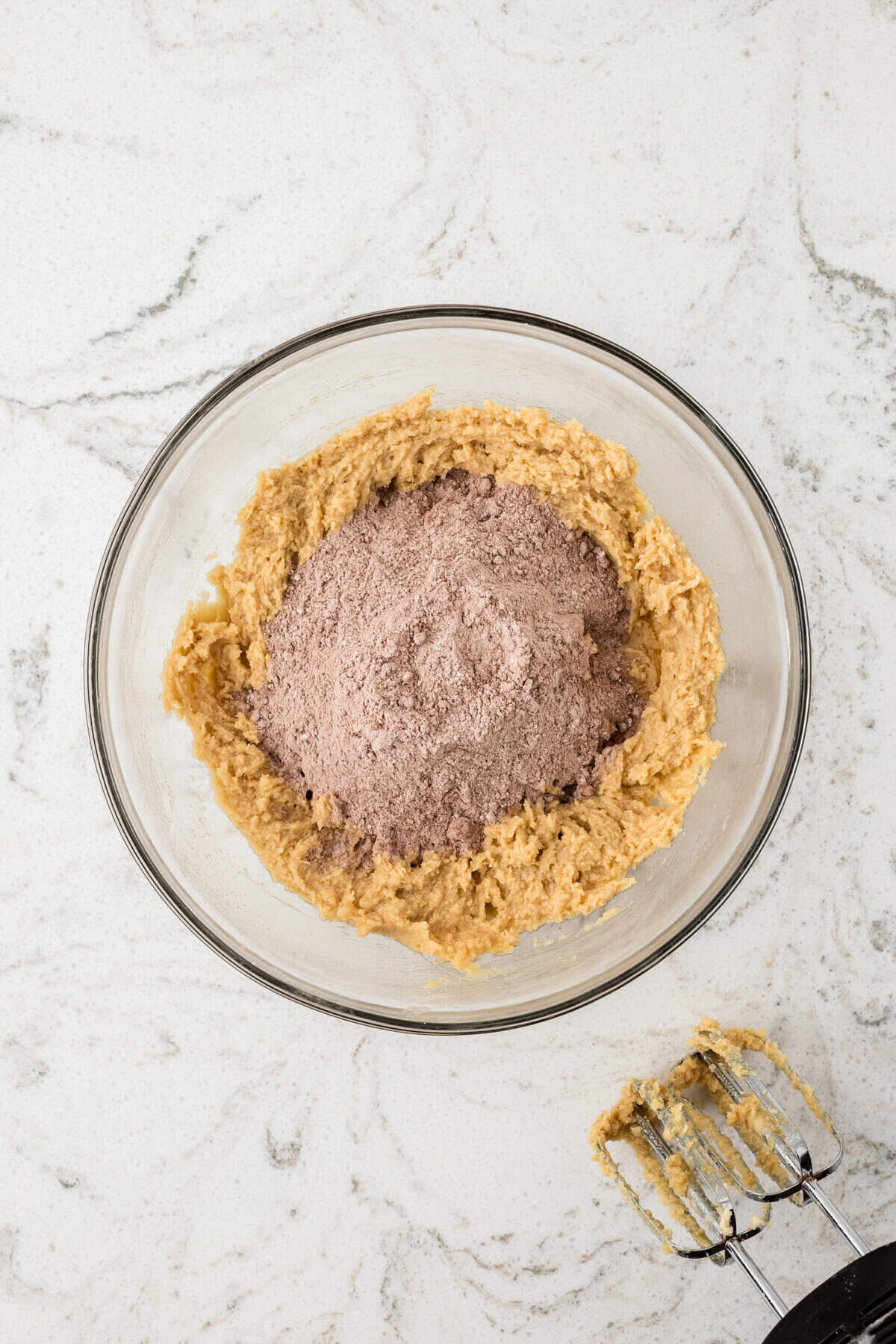 A bowl with the dry cocoa mixture added on top of the butter mixture, before combining.