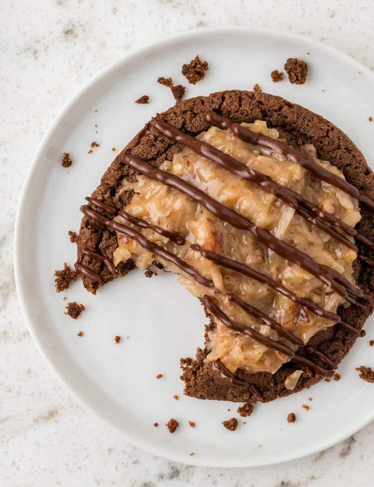 A single German chocolate cookie on a white plate with a bite taken out, showing the texture inside. Crumbs and smudges surround it.