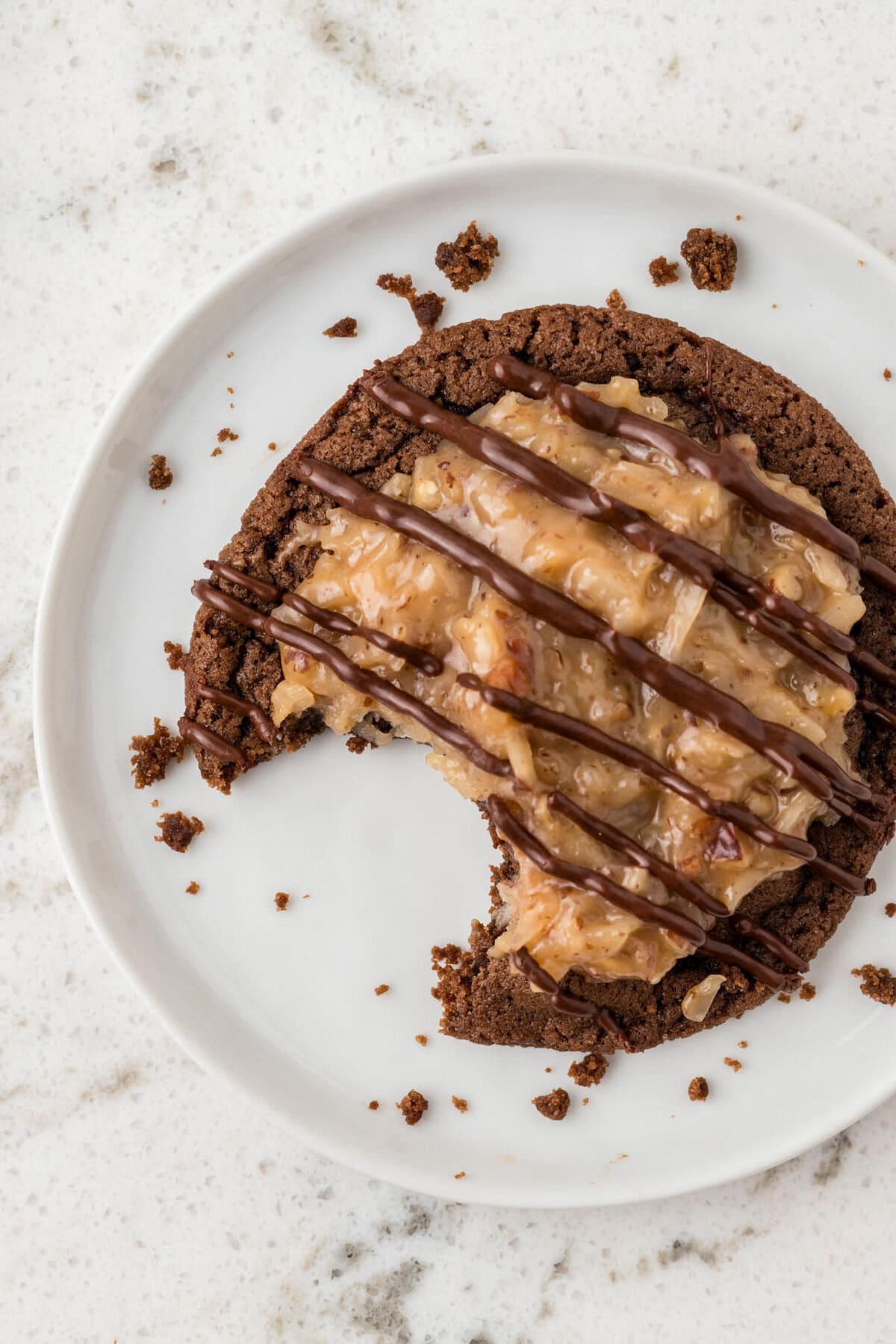  A single German chocolate cookie on a white plate with a bite taken out, showing the texture inside. Crumbs and smudges surround it.