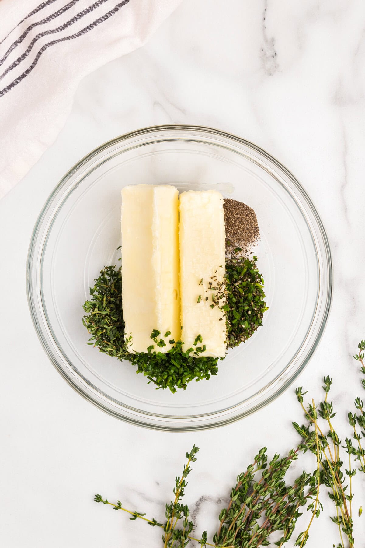 Overhead picture of herb butter ingredients in glass bowl unmixed.