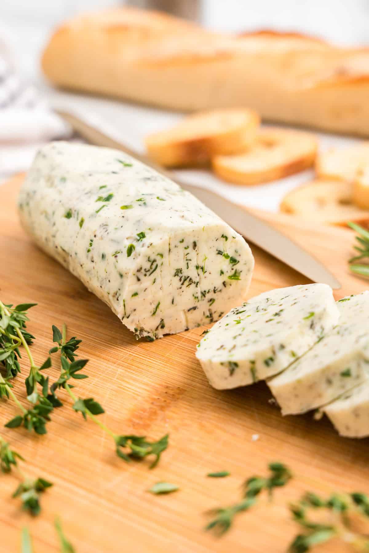 Herb Butter cut in slices on a cutting board with knife and herbs around it