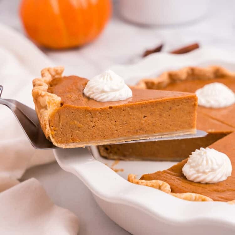 Slice of pumpkin pie lifted from the dish with a pie server, topped with whipped cream.