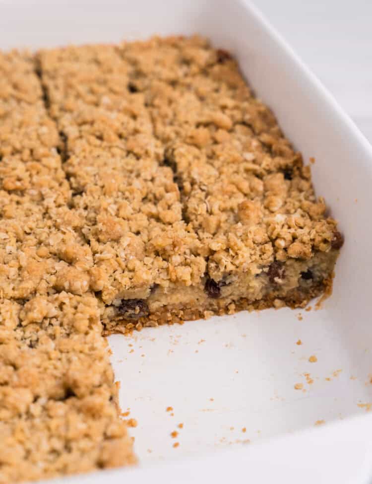 Side view of the pan with several bars removed, revealing the inside layers of the oat crust, creamy raisin filling, and crumble topping.
