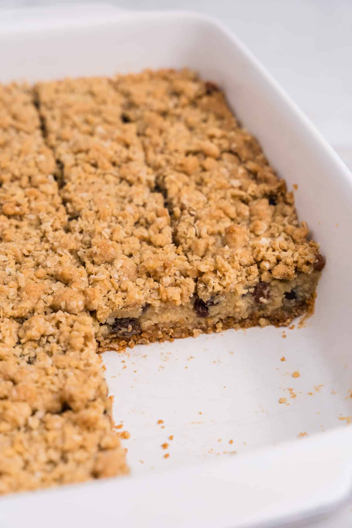 Side view of the pan with several bars removed, revealing the inside layers of the oat crust, creamy raisin filling, and crumble topping.