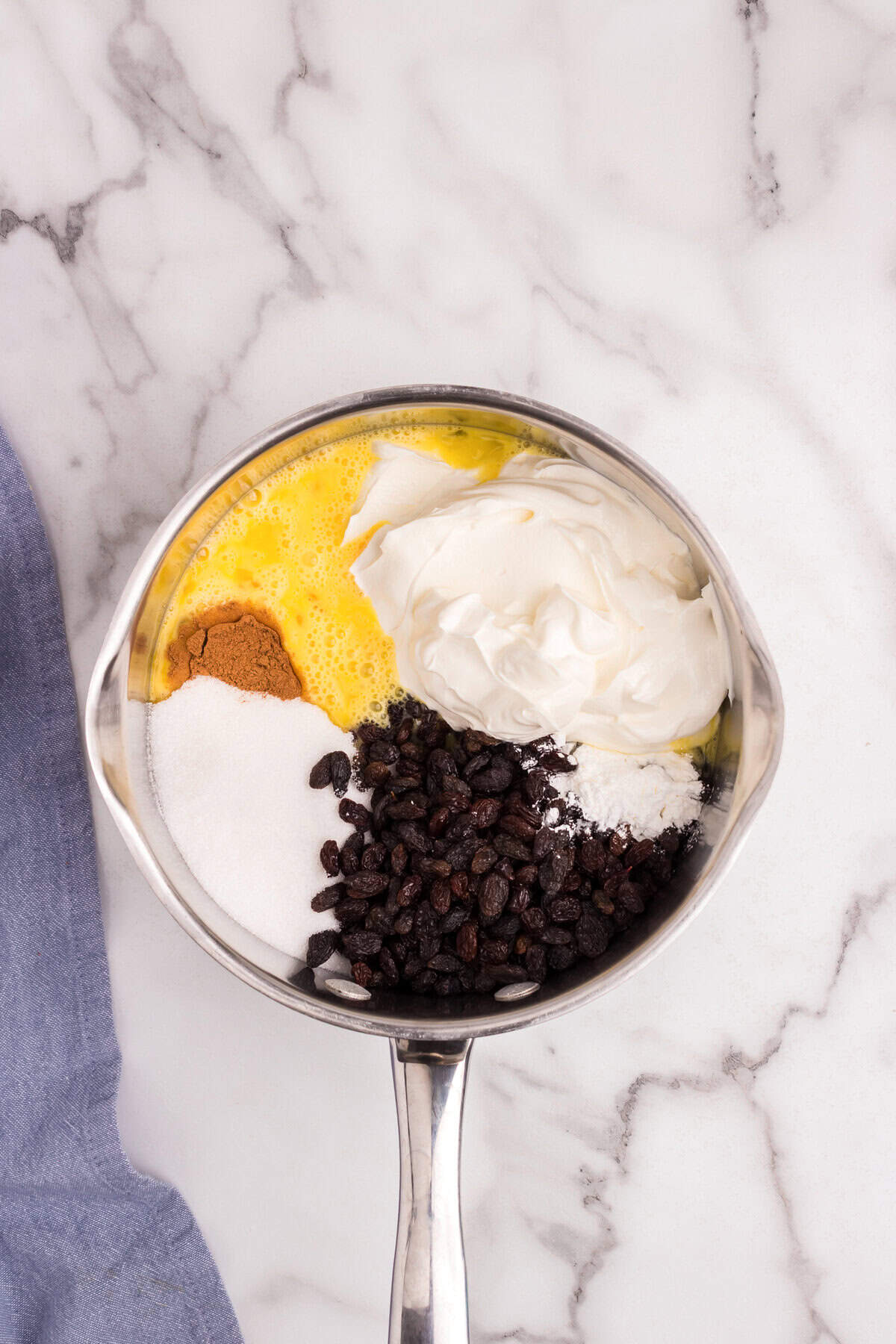 A saucepan filled with sour cream, raisins, sugar, cinnamon, cornstarch, and beaten eggs, unmixed.