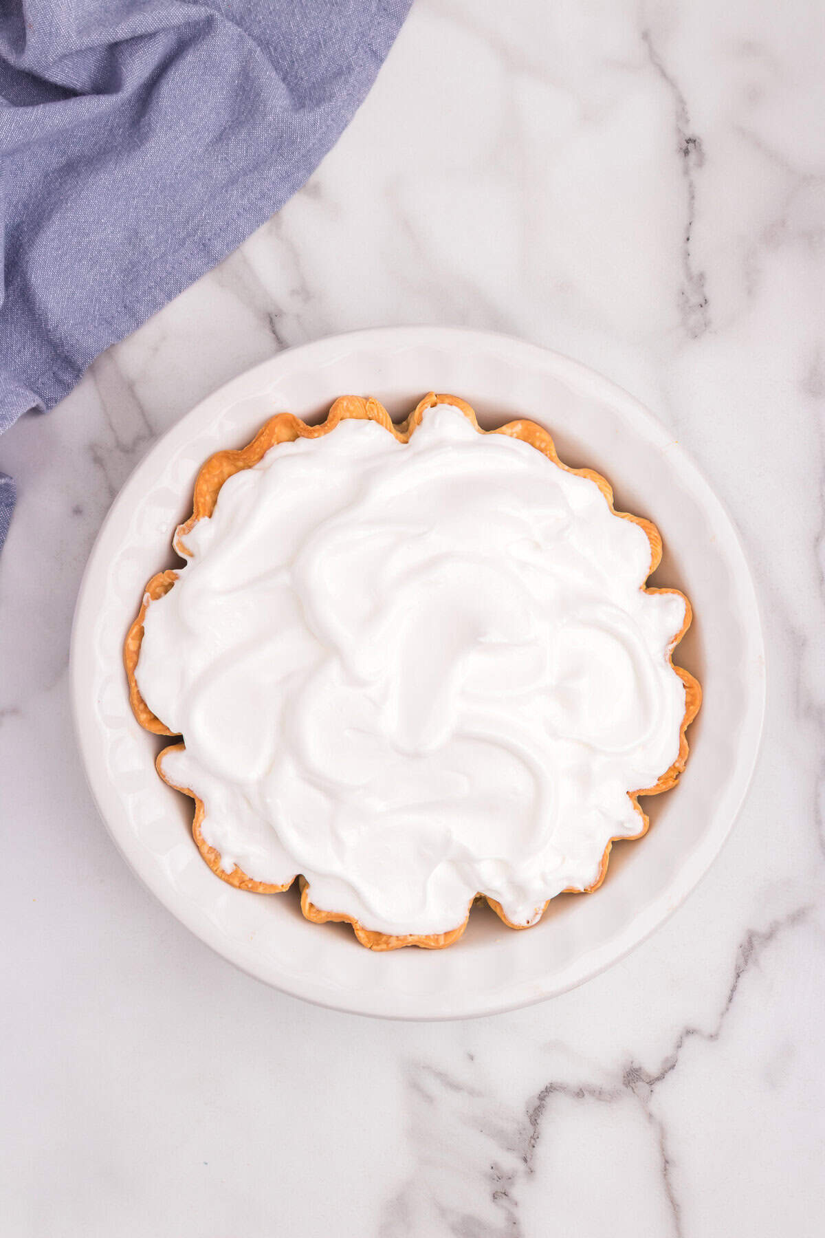 The custard-filled pie is fully covered with fluffy white meringue.