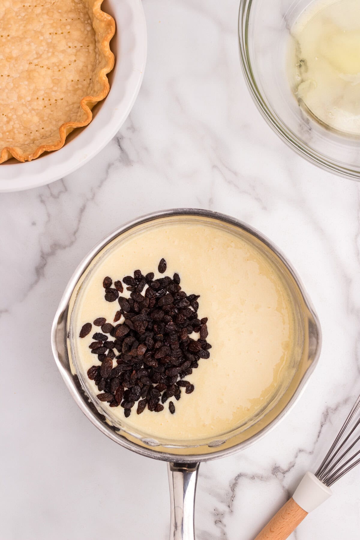 A saucepan filled with yellow custard mixture topped with a handful of raisins before being stirred.
