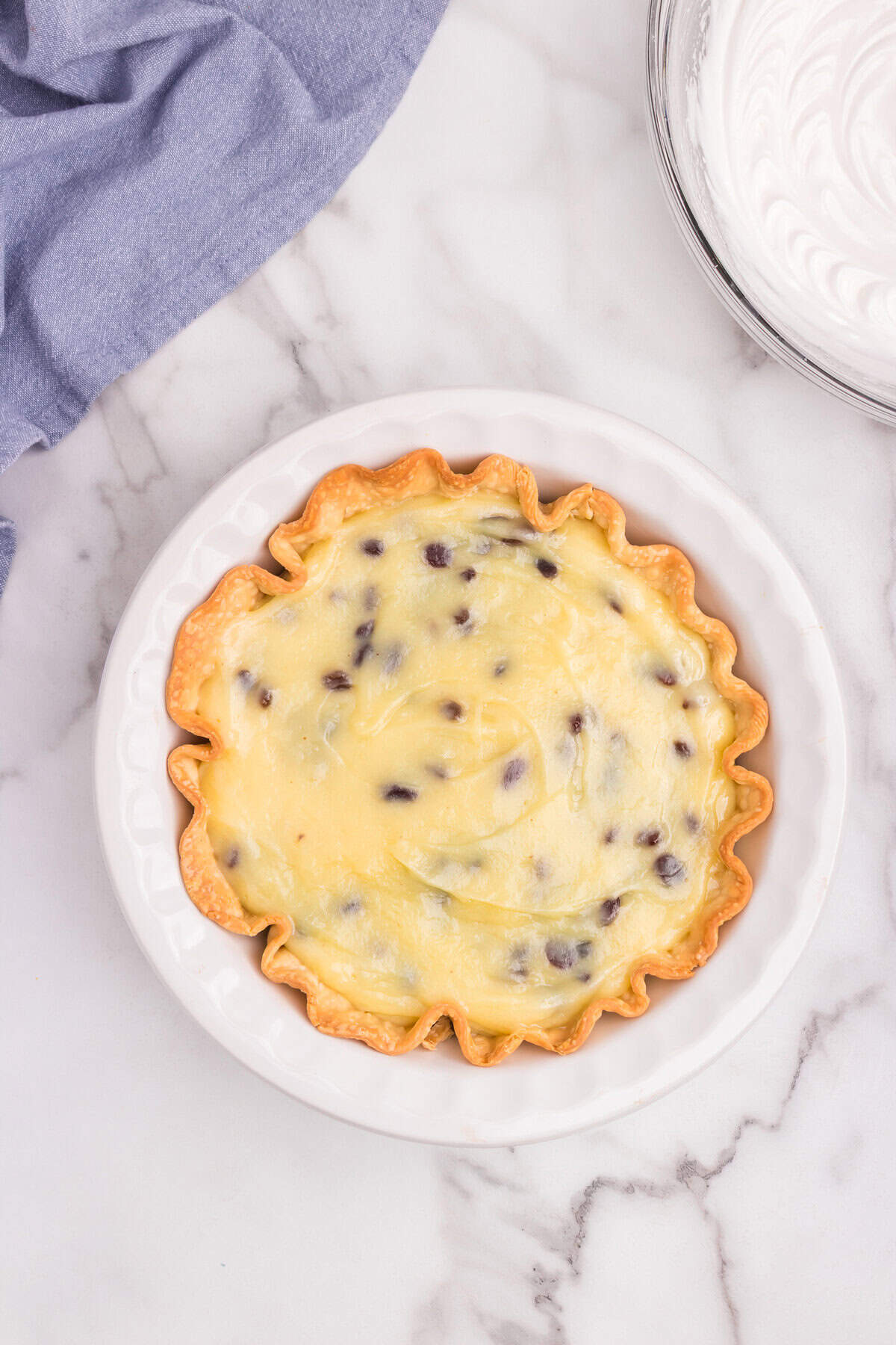 The baked pie crust is filled with the yellow custard mixture with visible raisins.
