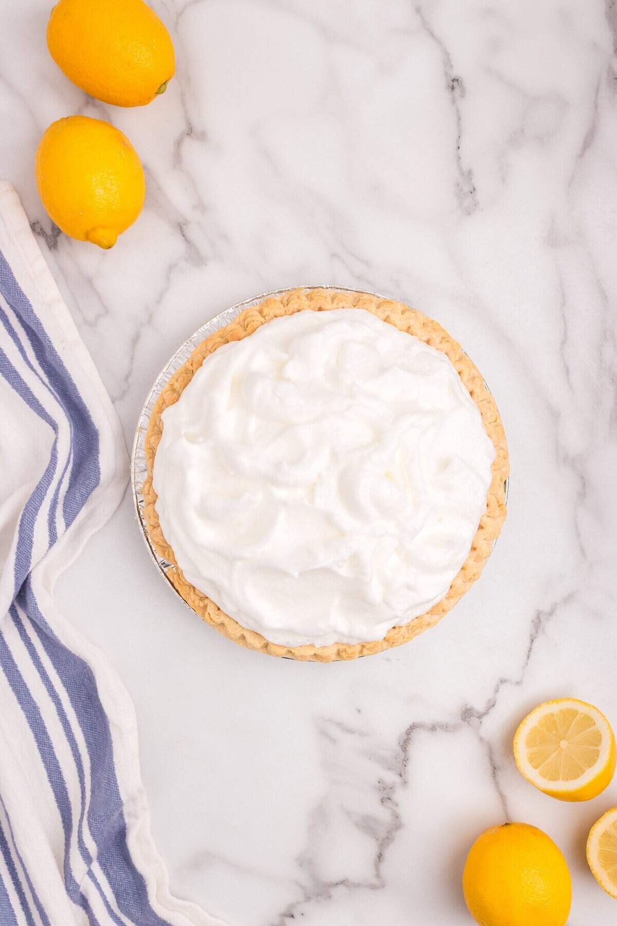 Unbaked lemon meringue pie with fluffy meringue piled high on top of lemon filling, ready for the oven. Whole and halved lemons placed beside the pie.