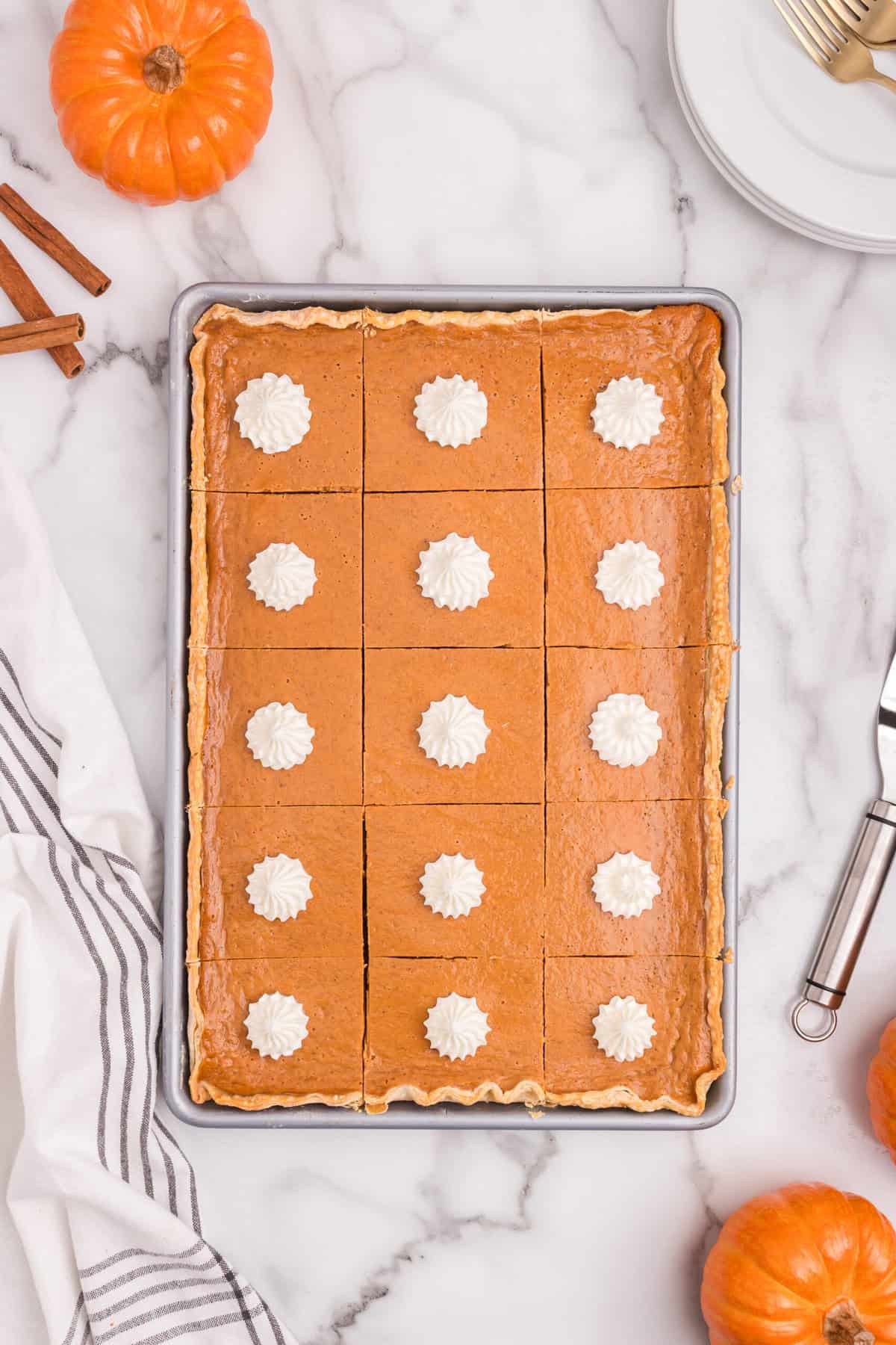 Pumpkin pie bars topped with dollops of whipped cream, arranged in the baking pan.