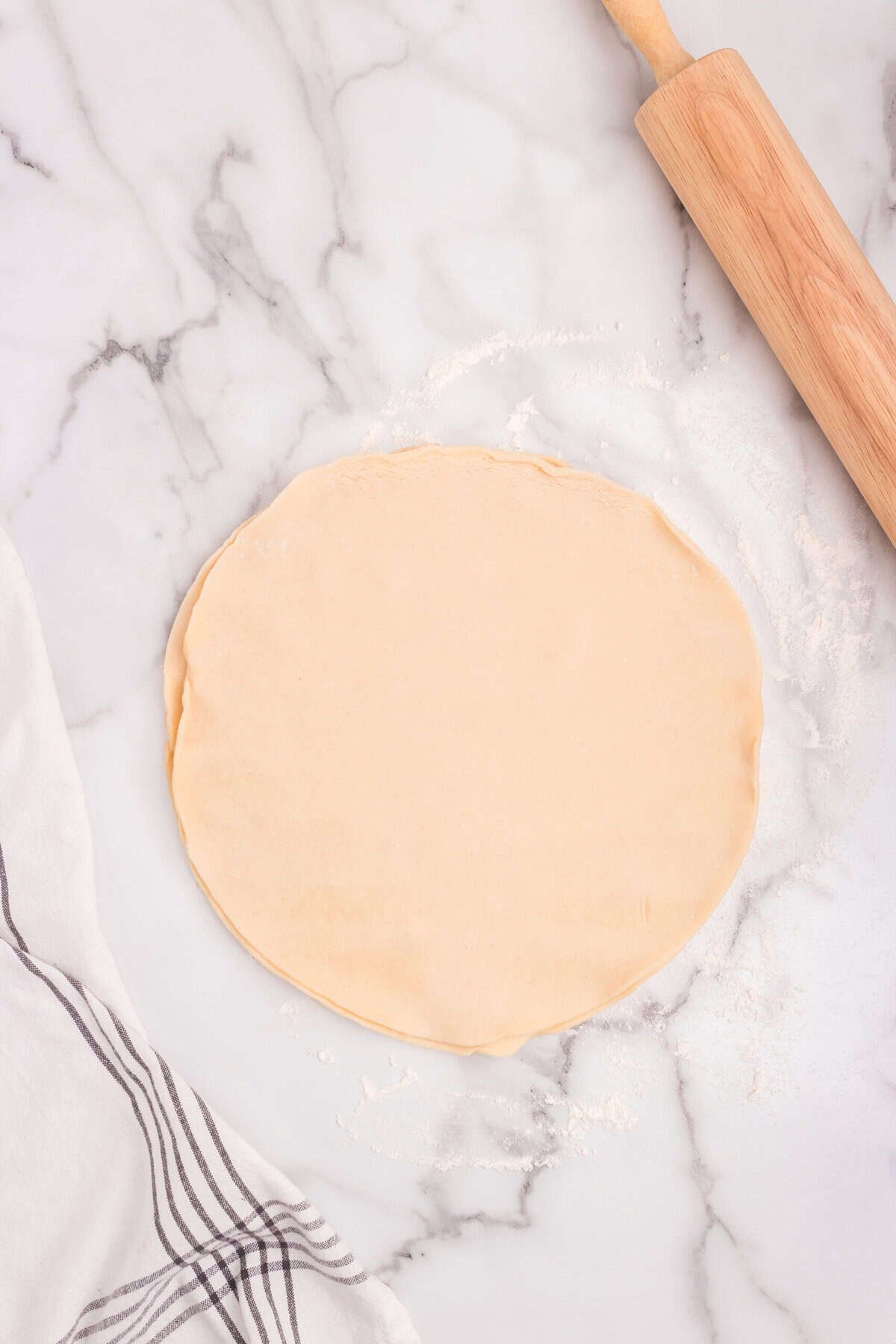 Round sheet of pie dough rolled out on a floured marble surface with a rolling pin beside it.