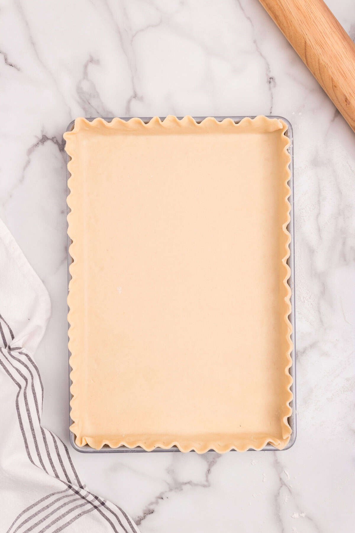Rectangular baking pan lined with pie crust, edges crimped neatly.