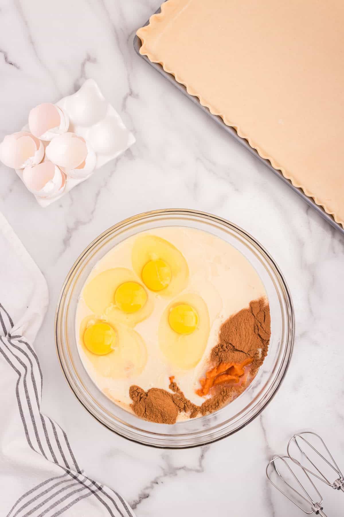 Mixing bowl with eggs, pumpkin puree, spices, and evaporated milk, ready to be blended.