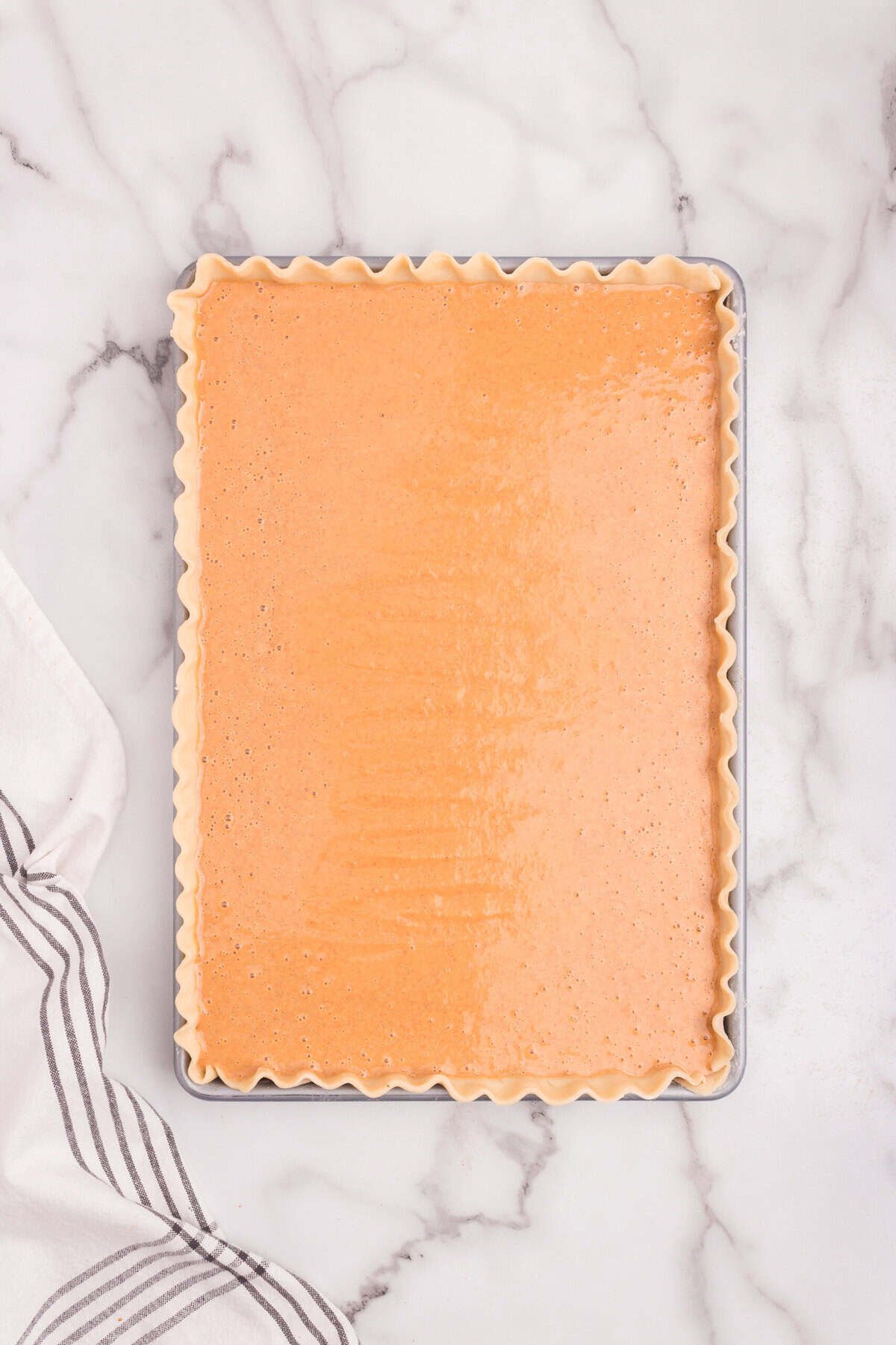 Raw pumpkin pie filling poured evenly into the prepared crust in the rectangular baking pan.